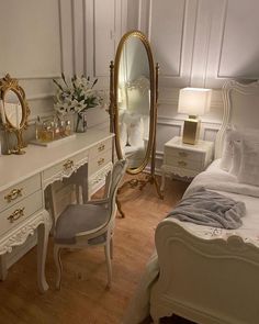 a bedroom with white furniture and gold accents on the walls, along with a large mirror