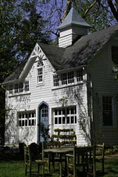 an old white house with tables and chairs in the front yard, on a sunny day