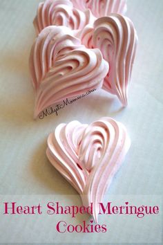 three heart shaped meringue cookies sitting on top of a white tablecloth with pink icing