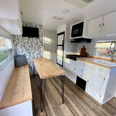 a kitchen and dining area in an rv with white cabinets, wood flooring and black appliances