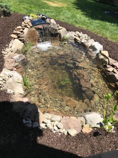 a small pond surrounded by rocks and gravel in the middle of a yard with water coming out of it