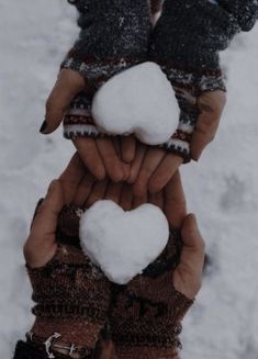 two hands holding snowballs in the shape of hearts, with one person wearing mittens and gloves