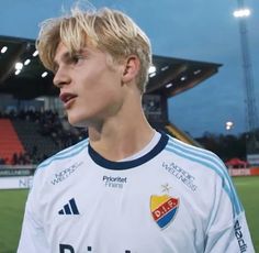 a young man standing on top of a soccer field wearing a white shirt and blue shorts