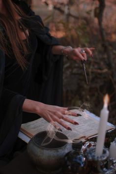 a woman in black dress holding a knife over a table with candles and other items on it