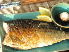 a fish is sitting on a plate next to some lemon wedges and a small bowl