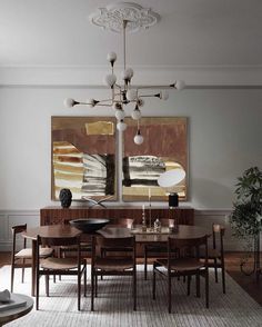 a dining room table and chairs in front of two paintings on the wall above it