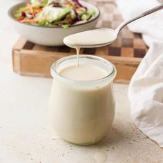 a spoon full of milk being poured into a glass jar with salad in the background