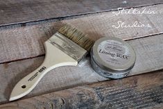 a paint brush sitting on top of a wooden table next to a tin of wax