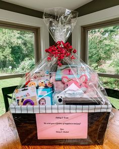 a basket filled with lots of toys on top of a wooden table next to two windows