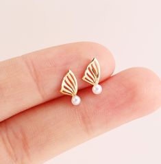 a pair of gold earrings with white pearls on the tip of each ear, sitting in someone's hand