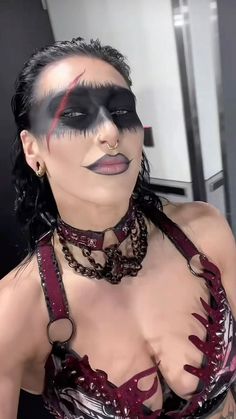 a woman with black and red makeup on her face wearing a mask, chains and choker