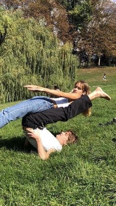 a man and woman laying on the grass with their arms around each other while one holds his leg up in the air