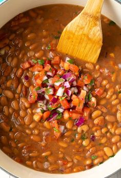 a pot filled with beans, onions and carrots next to a wooden spatula