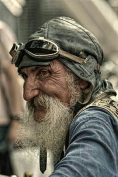 an old man with a long beard wearing goggles and a leather hat is looking at the camera