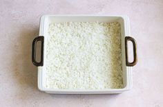 a square white dish filled with rice on top of a pink tablecloth covered floor