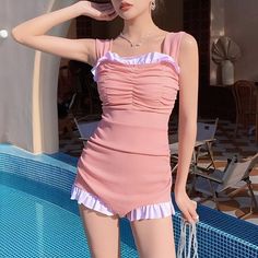 a woman standing next to a swimming pool wearing a pink dress and holding a white bag