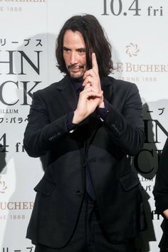 a man with long hair giving the peace sign while standing in front of a wall