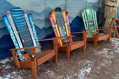 three wooden chairs with skis on them sitting in front of a wall painted with mountains