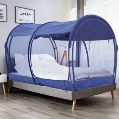 a bed with a blue canopy over it in a room that has hardwood floors and white walls