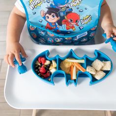 a toddler is eating lunch at the table with his lunch bag and spoons