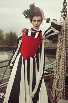 a woman in black and white striped dress holding a red heart on a boat deck