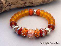 "A beautiful OrGaNiC bracelet of my handmade lampwork beads in orange and silver glass. Length is 7.50\".  Each larger round bead is roughly .50\" (12 mm) in diameter. Swarovski crystals and sterling silver Bali spacers accent this piece. This bracelet is strung on Stretch Magic and triple knotted for a secure bracelet. I want you to be happy with my lampwork bracelets. Please contact me if there are any problems and I will do my best to remedy it. If you are still not happy, you may return the bracelet (within 7 days) for a full refund. I understand from time to time glass beads can break. If any of my lampwork beads ever break, I would be happy to repair them free of charge, minus any shipping charges. Please contact me for details. I use Moretti Italian glass, Double-Helix, R4, CIM, Kug Handmade Orange Spiritual Bracelets, Handmade Orange Stretch Bracelet With Round Beads, Handmade Orange Bead Stretch Bracelet, Handmade Spiritual Orange Stretch Bracelet, Orange Polished Beads Bracelet, Orange Bracelets With Colorful Beads For Jewelry Making, Orange Large Beads Bracelet, Gift Orange Stretch Bracelet With Large Beads, Orange Stretch Bracelet With Large Beads As Gift