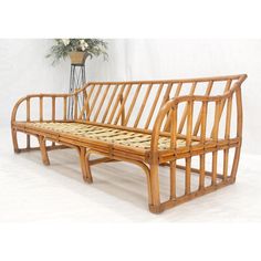 a wooden bench sitting next to a plant on top of a white floor covered in wicker