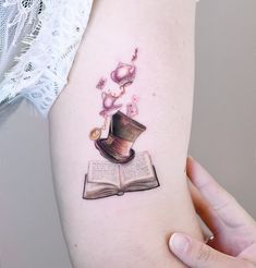 a woman's arm with an open book and hat tattoo on the left side of her body