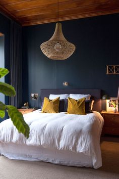 a bedroom with blue walls, white bedding and yellow pillows on the headboard