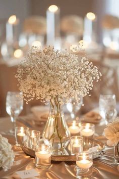 a vase filled with white flowers sitting on top of a table next to glasses and candles