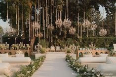 an outdoor ceremony with white couches and greenery on the ground, surrounded by hanging chandeliers