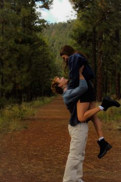 a man carrying a woman on his back in the middle of a dirt road surrounded by trees