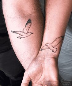 two people holding hands with tattoos on their arms and one has a seagull tattooed on the arm