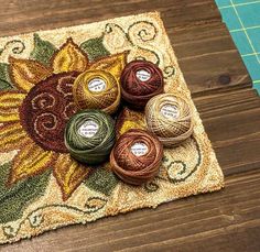 four balls of yarn sitting on top of a wooden floor next to a mat with an image of a sunflower