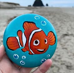 a hand holding up a painted rock with an image of a clown fish on it