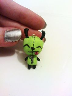 a person's hand holding a small green toy with black eyes and horns on it