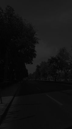 an empty street at night with trees on both sides and dark clouds in the sky