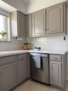 a kitchen with gray cabinets and white counter tops, an open dishwasher in the middle