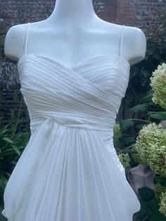 a white dress is on display in front of some flowers