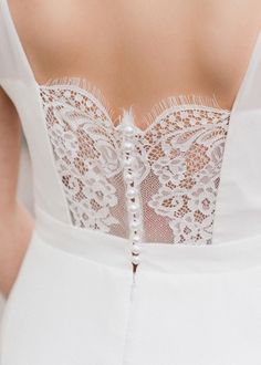 the back of a woman's wedding dress with white lace and buttons on it