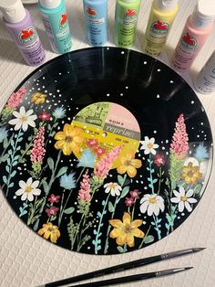 a plate with flowers painted on it next to paintbrushes and other items that include acrylic