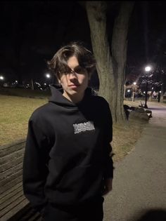 a young man standing in front of a park bench at night wearing a black hoodie