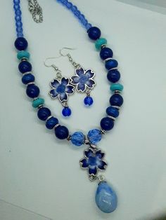 This beautiful set features blue and white flowers in the earrings and the main pendant of the necklace.  The necklace features different shades of blue beads to compliment the pendant. This is a great statement piece to set off any outfit and a must-have for women who want a unique necklace to show their personal style. Depending on the size, all jewelry comes shipped in either a box with cotton padding or wrapped carefully in tissue paper and mailed in a thick padded envelope to ensure it reac Blue Beaded Flower Jewelry, Blue Flower-shaped Beaded Jewelry, Blue Beaded Round Beads Jewelry Sets, Blue Beaded Jewelry Sets With Round Beads, Blue Beaded Necklace With Flower Pendant, Blue Flower Pendant Beaded Necklace, Bohemian Blue Flower Necklace, Blue Beaded Jewelry Sets For Gift, Blue Jewelry Sets With Round Beads As A Gift