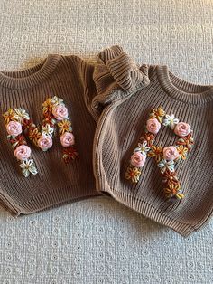 two knitted sweaters with flowers on them are laying on the floor next to each other