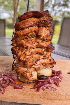 a stack of meat sitting on top of a wooden cutting board next to an onion