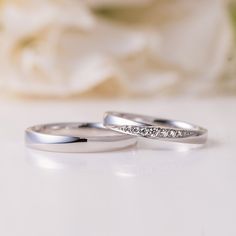 two wedding rings sitting on top of a table next to a white rose and flower