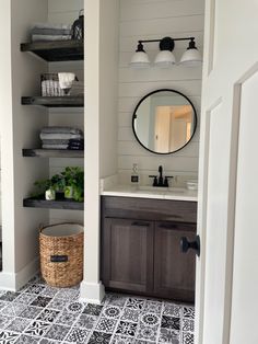 a bathroom with black and white tile flooring next to a wooden sink vanity topped with a round mirror