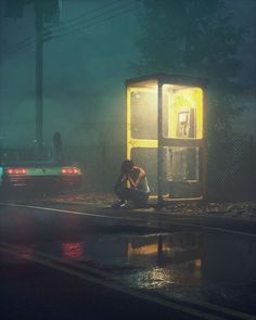 a man sitting on the side of a road next to a phone booth at night