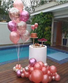 some pink and gold balloons are on the ground near a pool with a cake in it