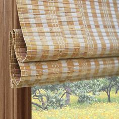 a close up of a bamboo blinds with trees in the background and yellow flowers on the window sill